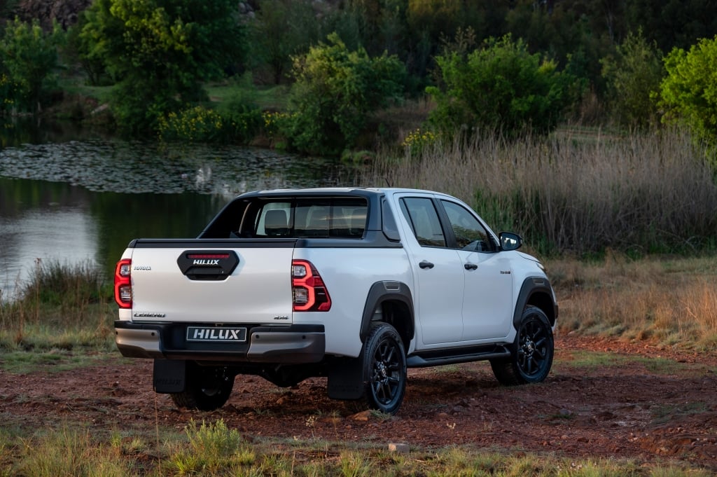 White Hilux next to a dam with tress in the background