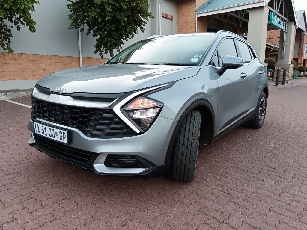 Front 3 quarter view of a Sparkling Silver Kia Sportage LX in a shopping centre parking lot
