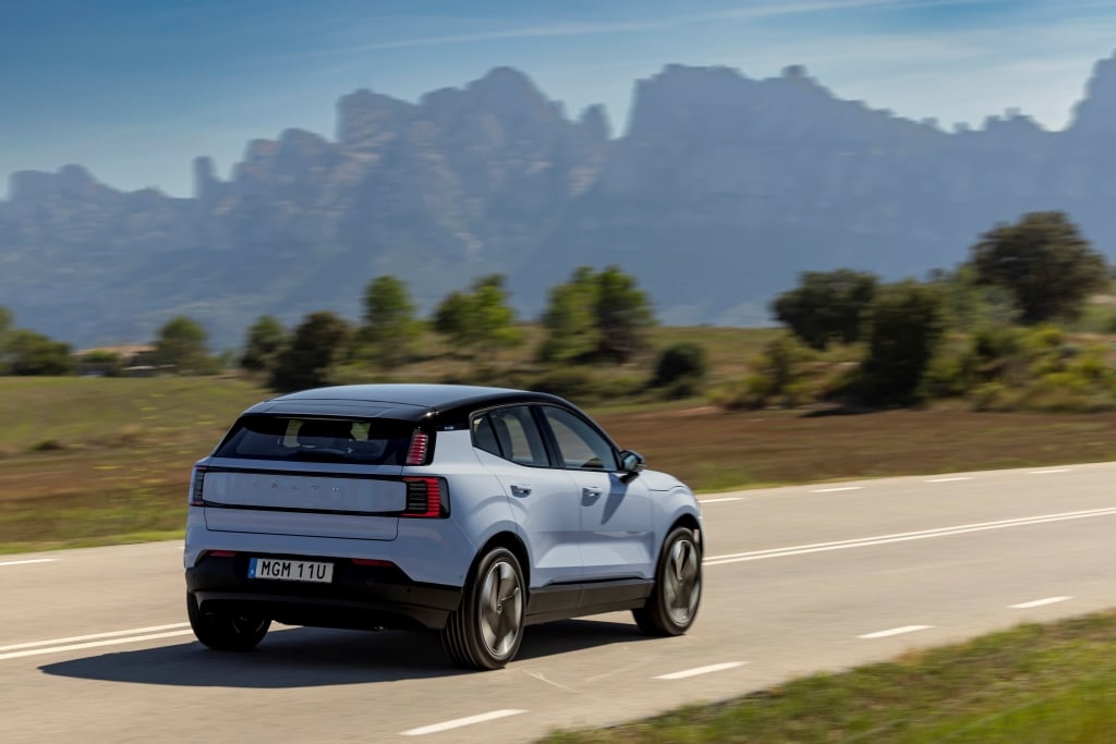 Rear view of a Volvo EX30 driving on a road with mountains in the background